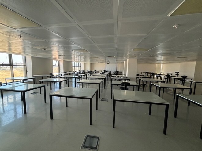 L119 Çizim Atölyesinde geniş aralıklarla yerleştirilmiş cam yüzeyli çizim masaları ve çalışma koltukları.
