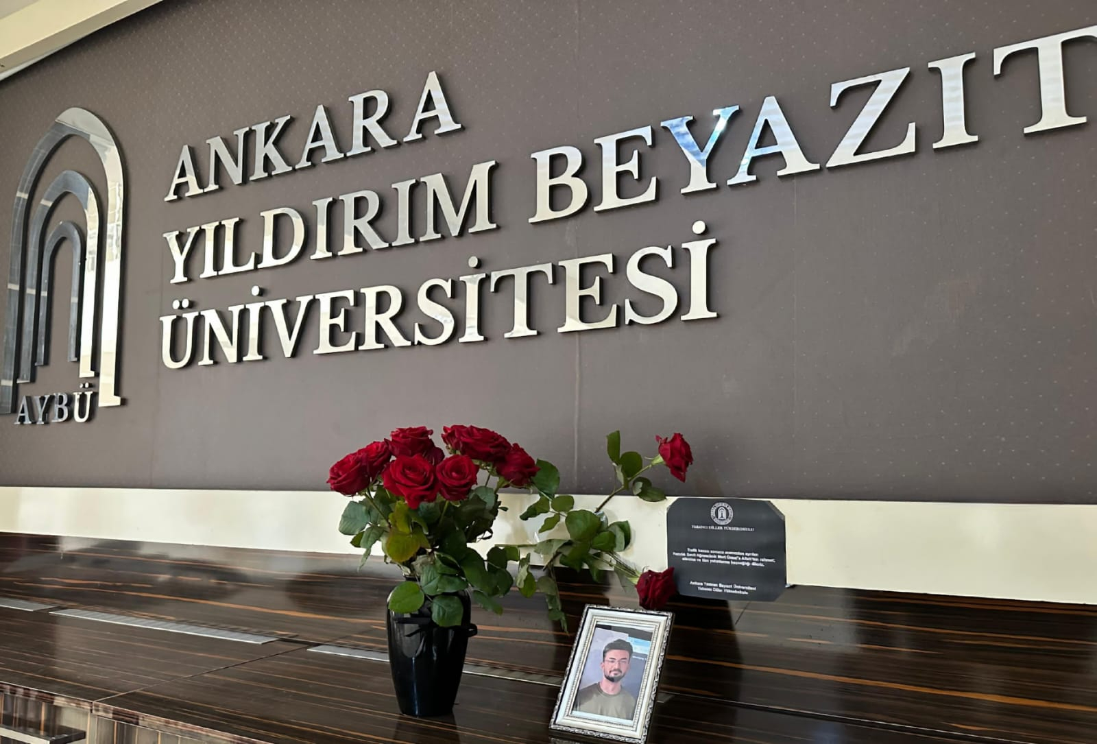 Yabancı Diller Yüksekokulu zemin katta Mert Ünsal'ın  fotoğrafı ve bırakılan çiçek fotoğrafı