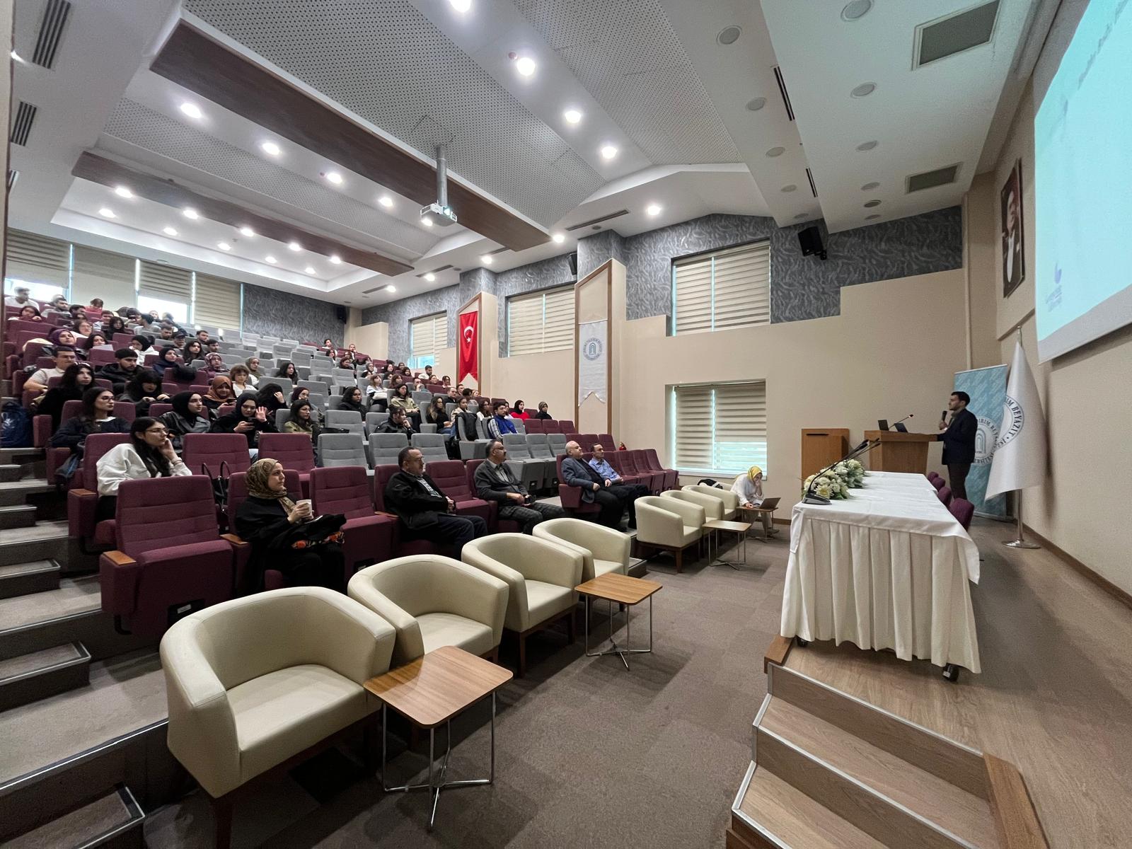 Dr. Öğretim Üyesi Serdar Aydın konuşmasını yaparken salonun ve dinleyicilerin fotoğrafı.